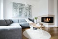 Grey corner settee with blankets standing in white Nordic living room interior with fresh tulips, books and tea cup on hairpin tab