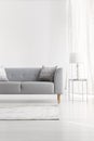 Grey couch next to lamp on silver table in white flat interior with copy space on empty wall. Real photo Royalty Free Stock Photo
