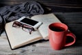 Grey cozy knitted scarf with cup of coffee or tea, phone, glasses and open book on a wooden table. Royalty Free Stock Photo