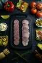 Grey cutting board with salami and ham. Around tomato, souce, olives, lemon, olive oil with spice and sandwiches Royalty Free Stock Photo