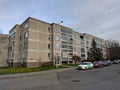 A grey four-story old block of flats on sidewalk and road with parked cars next to it