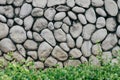 Grey or gray stone wall with natural texture round stone with low bush in the front. Natural stone old style wall. Royalty Free Stock Photo