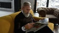 Grey hair man reading newspaper on sofa in flat