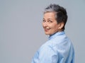 Grey hair mature woman posing standing back half turn looking over shoulder at camera and smile wearing blue shirt Royalty Free Stock Photo