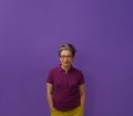 Grey hair senior woman posing with hands in pockets looking at camera wearing glasses, purple polo and mustard jeans Royalty Free Stock Photo