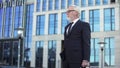 Grey-haired company director standing outdoors, confident businessman waiting