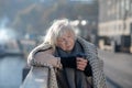 Grey-haired homeless woman standing on the bridge and drinking tea