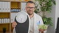 Grey-haired man dietician holding salad and weighing machine at the clinic