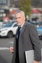 Grey-haired man wearing a grey coat looking tired