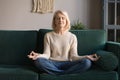 Grey haired mature woman meditating, practicing yoga at home