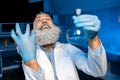 Grey haired scientist celebrating success of scientific experiment and holding flask with reagent Royalty Free Stock Photo