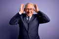 Grey haired senior business man wearing glasses and elegant suit and tie over purple background Doing bunny ears gesture with Royalty Free Stock Photo