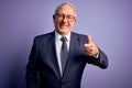 Grey haired senior business man wearing glasses and elegant suit and tie over purple background doing happy thumbs up gesture with Royalty Free Stock Photo