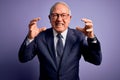 Grey haired senior business man wearing glasses and elegant suit and tie over purple background Shouting frustrated with rage, Royalty Free Stock Photo