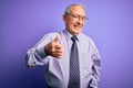 Grey haired senior business man wearing glasses standing over purple isolated background doing happy thumbs up gesture with hand Royalty Free Stock Photo