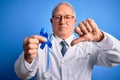 Grey haired senior doctor man holding colon cancer awareness blue ribbon over blue background with angry face, negative sign Royalty Free Stock Photo