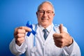 Grey haired senior doctor man holding colon cancer awareness blue ribbon over blue background happy with big smile doing ok sign, Royalty Free Stock Photo
