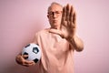 Grey haired senior football player man holding soccer ball over pink isolated background with open hand doing stop sign with