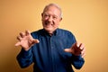 Grey haired senior man wearing casual blue shirt standing over yellow background smiling funny doing claw gesture as cat, Royalty Free Stock Photo