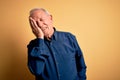 Grey haired senior man wearing casual blue shirt standing over yellow background Yawning tired covering half face, eye and mouth Royalty Free Stock Photo