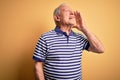 Grey haired senior man wearing casual navy striped t-shirt standing over yellow background shouting and screaming loud to side Royalty Free Stock Photo