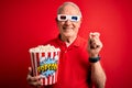 Grey haired senior man wearing 3d movie glasses and eating popcorn over red background with a happy face standing and smiling with Royalty Free Stock Photo