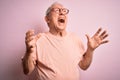 Grey haired senior man wearing glasses standing over pink isolated background crazy and mad shouting and yelling with aggressive Royalty Free Stock Photo