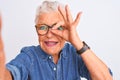 Grey-haired woman wearing denim shirt and glasses make selfie over isolated white background with happy face smiling doing ok sign Royalty Free Stock Photo