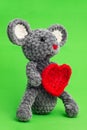 Grey knitted mouse with a heart in hand on a green background, side view Royalty Free Stock Photo