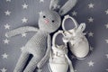 Grey knitted toy rabbit, and children`s white shoes are on grey background Royalty Free Stock Photo