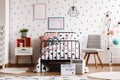 Grey knot pillow and pastel pink pillow on industrial single bed in scandinavian bedroom interior with grey chair, wooden