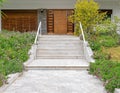 Grey marble paved corridor to a house entrance stairs with a natural brown wood door. Royalty Free Stock Photo