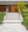 Grey marble paved corridor to a house entrance stairs with a natural brown wood door. Royalty Free Stock Photo