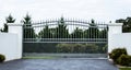 Grey metal wrought iron driveway property entrance gates set in white concrete brick fence, garden trees in background