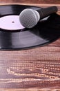 Grey microphone and vinyl record on wooden background.