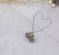 Grey pendant flower earrings in the shape of a flower.Earrings are flanked by cardboard, floral specimens and other ornaments