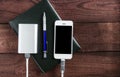 Grey phone and power bank connected by cord with pen and notebook on a wooden background Royalty Free Stock Photo