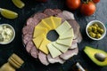 Grey plate with cheese and mozzarella on a black background, around the salami and ham, tomato, souce, olives, lemon, olive oil Royalty Free Stock Photo