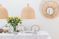 Plates, vine glasses and yellow flowers in vase in trendy dining room interior with wicker chandeliers