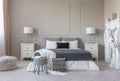 Grey pouf with open book in the food of king size bed with grey and white bedding, copy space on empty wall