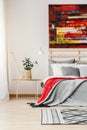 Grey and red blanket on bed next to table with lamp and plant in Royalty Free Stock Photo