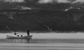 Grey-scale shot of a fisherman on the boat in the lake with mountains in the background