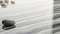 Smooth grey pebble rests on a polished reflective surface with swirling marbled patterns of blue green and beige Royalty Free Stock Photo