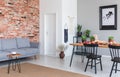 Grey sofa against red brick wall in flat interior with poster and black chairs at dining table. Real photo Royalty Free Stock Photo