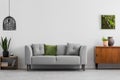Grey sofa with pillows next to wooden cupboard in living room interior with lamp and poster. Real photo Royalty Free Stock Photo