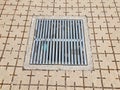 Grey square floor tiles with lines on ground with metal drain