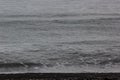 Grey surface sea in overcast weather with dots of drops of rain and thin line of black volcanic beach as line, texture, background Royalty Free Stock Photo