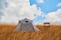 Grey tent and chair on dry grass. Empty meadow for rest. Fresh air and new adventure. Virgin nature and camping concept Royalty Free Stock Photo