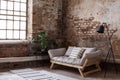 Grey wooden couch between plant and lamp in loft interior with red brick wall and window Royalty Free Stock Photo