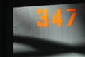 Grey wooden wall and the number 347 written on it with bright orange color